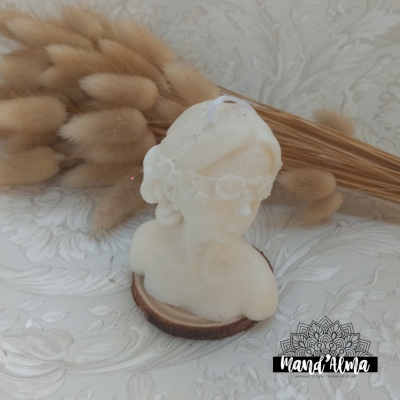Vela branca em forma de busto feminino com coroa de flores sobre base de madeira