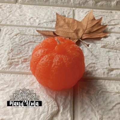 Vela laranja em forma de tangerina com folha seca castanha sobre fundo branco texturado.