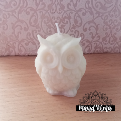 Vela branca em forma de coruja com textura detalhada sobre superfície de madeira e fundo rosa