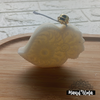 Vela branca com padrão floral em relevo e sino dourado, sobre bandeja de madeira