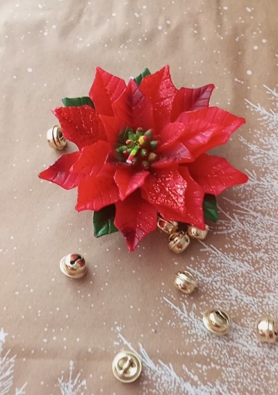 Flor de Natal vermelha artificial com pequenos sinos dourados em fundo bege com padrão de neve