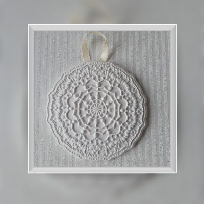 Toalha redonda branca em crochê com padrão circular pendurada por fita creme