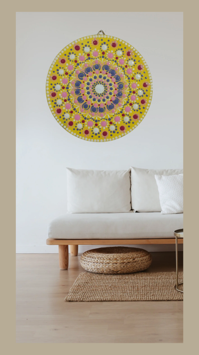 Objeto decorativo redondo amarelo com padrões coloridos pendurado numa parede acima de um sofá branco