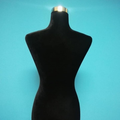 Manequim feminino preto com suporte metálico e base de madeira contra fundo azul