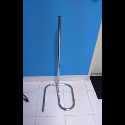 Suporte de metal cromado com base oval e haste vertical em chão branco e parede azul