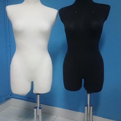 Dois manequins femininos branco e preto com suportes metálicos em chão de azulejos brancos e parede azul