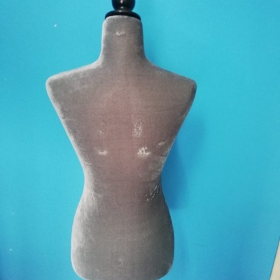 manequim de costura cinzento com suporte em madeira preta contra parede azul