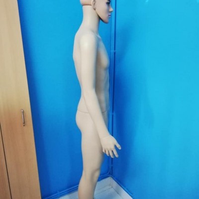 Mannequim masculino em plástico bege junto a parede azul e móvel de madeira clara
