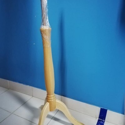 Suporte de manequim de madeira clara com base de três pernas, parcialmente envolvido em plástico, junto a uma parede azul