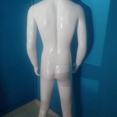 Mannequim masculino branco visto de costas num canto com paredes azuis.