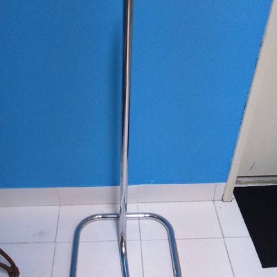 Suporte metálico cromado com tubo em formato retangular em chão branco junto a parede azul