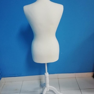 Manequim feminino branco com base branca sobre chão de azulejos com parede azul