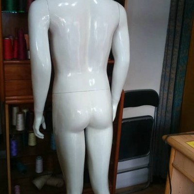 Manequim masculino branco visto de costas numa sala com linhas coloridas e cadeira preta.