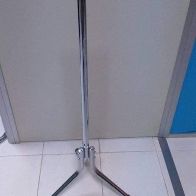 Suporte metálico cromado com três pés no chão ao lado de porta cinza e parede azul