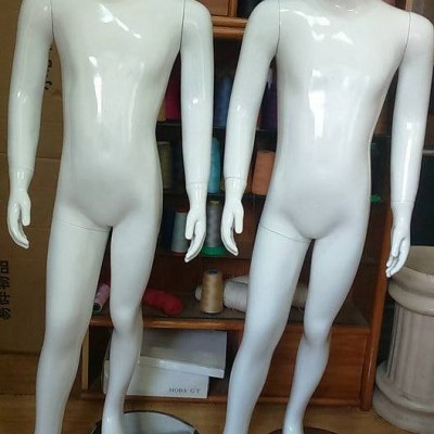 Dois manequins brancos de corpo inteiro em material plástico brilhante, sobre bases metálicas, com armário e linhas coloridas ao fundo