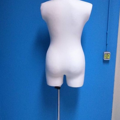 Manequim branco feminino em base metálica, contra parede azul