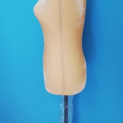 Manequim feminino de meio corpo bege com suporte preto e base, contra parede azul