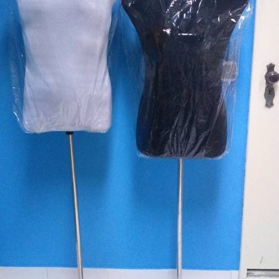 Dois manequins de torso, branco e preto, embalados em plástico, com base metálica em frente a parede azul