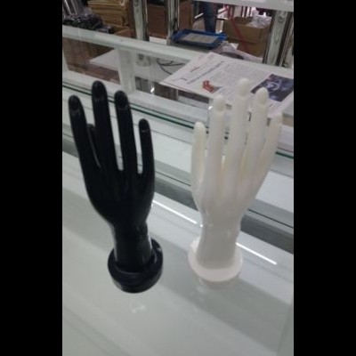 Duas esculturas de mãos em plástico preto e branco sobre mesa de vidro.