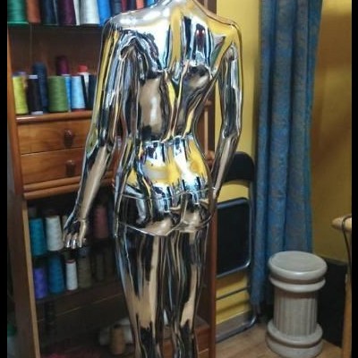 Maniquim cromado de corpo inteiro visto de costas em quarto com estante e carretéis de linha