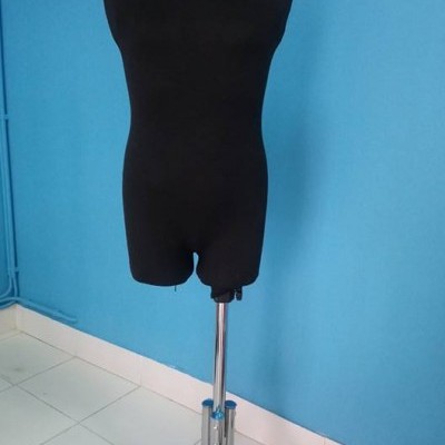 Manequim de costura preto sobre tripé metálico prateado com parede azul clara ao fundo