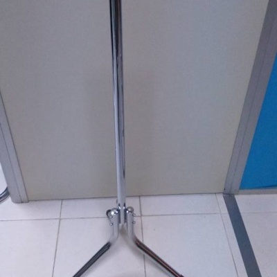 Suporte metálico cromado com três pés posicionado em chão de azulejos branco junto a porta clara