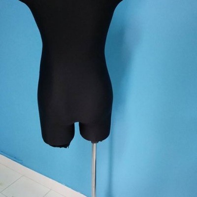 Manequim de costura preto com suporte metálico em tripé numa sala de parede azul