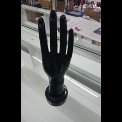 Mão de manequim preta sobre superfície branca com vidro e prateleiras ao fundo