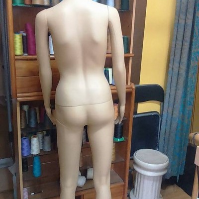 Mannequim feminino de costas em quarto com prateleira de linhas coloridas e cortina azul