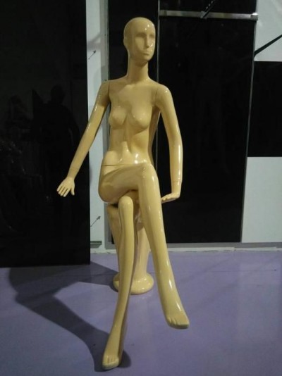 Mannequim feminino bege sentado com pernas cruzadas em superfície roxa