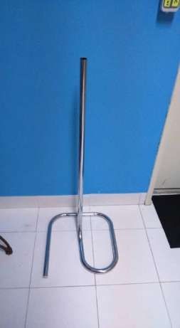 Suporte de metal cromado com base oval e haste vertical em chão branco e parede azul