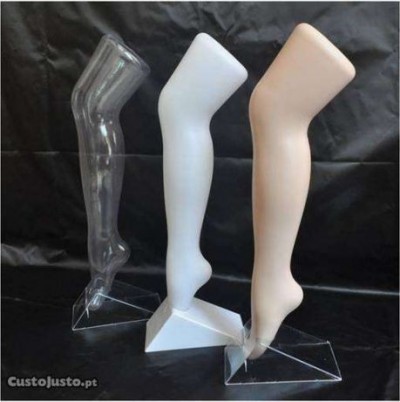 Três manequins de pernas femininas em plástico, uma transparente, uma branca e uma bege, com bases triangulares.