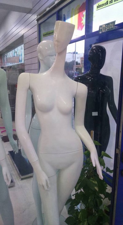 Mannequins femininos brancos, cinza claro e preto em loja com porta e planta ao fundo