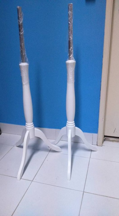 Dois manequins de madeira branca com hastes cobertas por plástico em chão de azulejos frente a parede azul