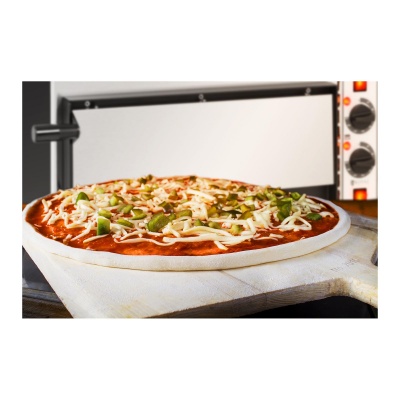 Pizza crua com queijo e molho sobre pá de madeira em frente a forno