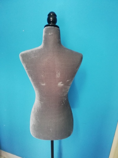 manequim de costura cinzento com suporte em madeira preta contra parede azul