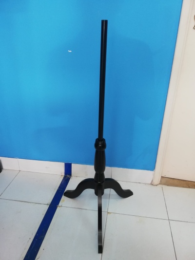 Suporte de madeira preta para instrumento ou microfone com base tripé em chão de azulejos brancos e parede azul