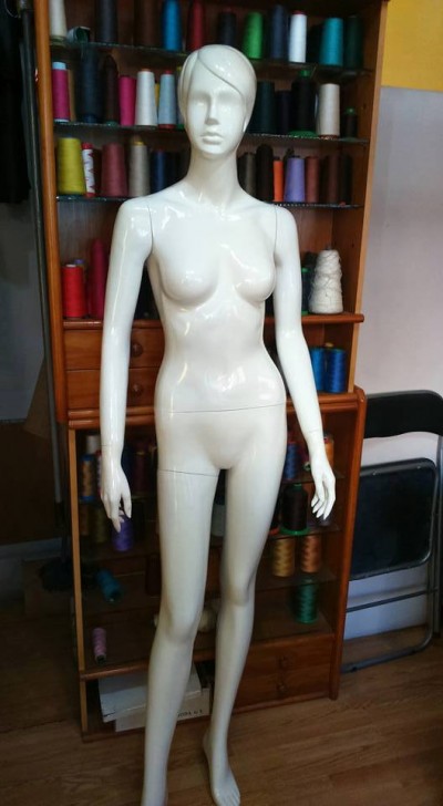 Mannequim feminino branco com bobinas de linha colorida ao fundo.