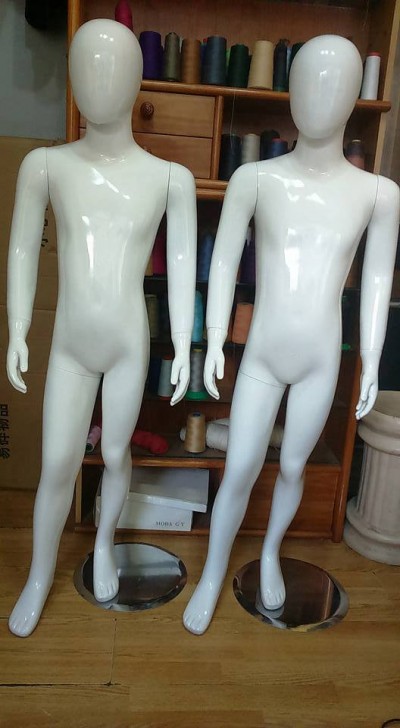 Dois manequins brancos de corpo inteiro em material plástico brilhante, sobre bases metálicas, com armário e linhas coloridas ao fundo