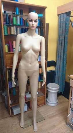 Mannequin feminino bege em sala com estante de linhas e cortina azul