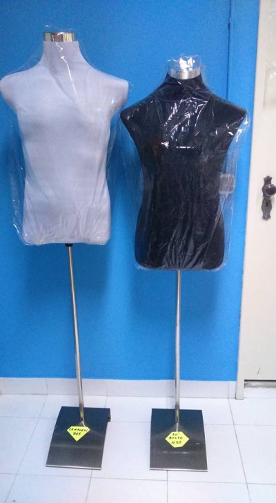 Dois manequins de torso, branco e preto, embalados em plástico, com base metálica em frente a parede azul
