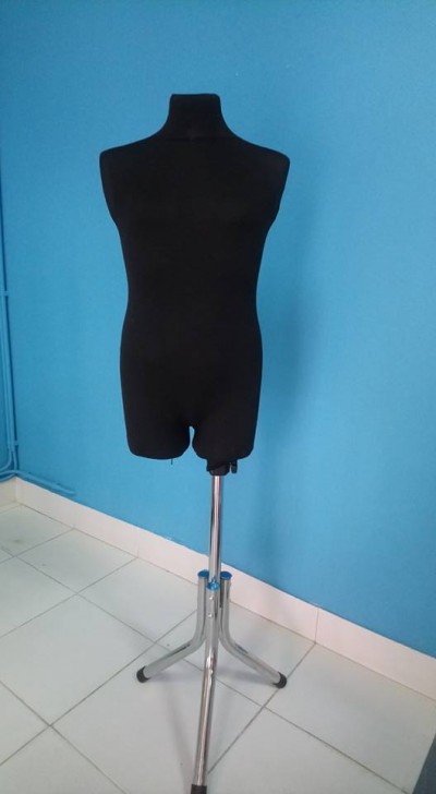 Manequim de costura preto sobre tripé metálico prateado com parede azul clara ao fundo