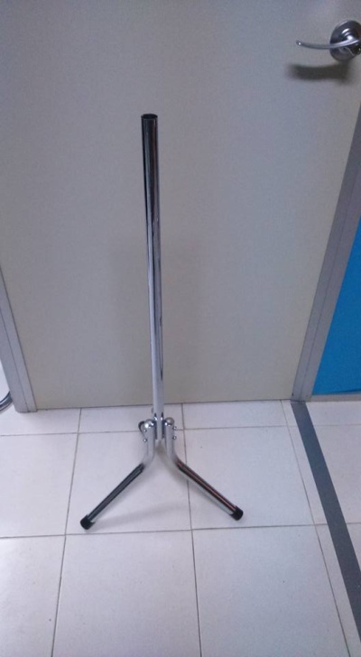 Suporte metálico cromado com três pés posicionado em chão de azulejos branco junto a porta clara