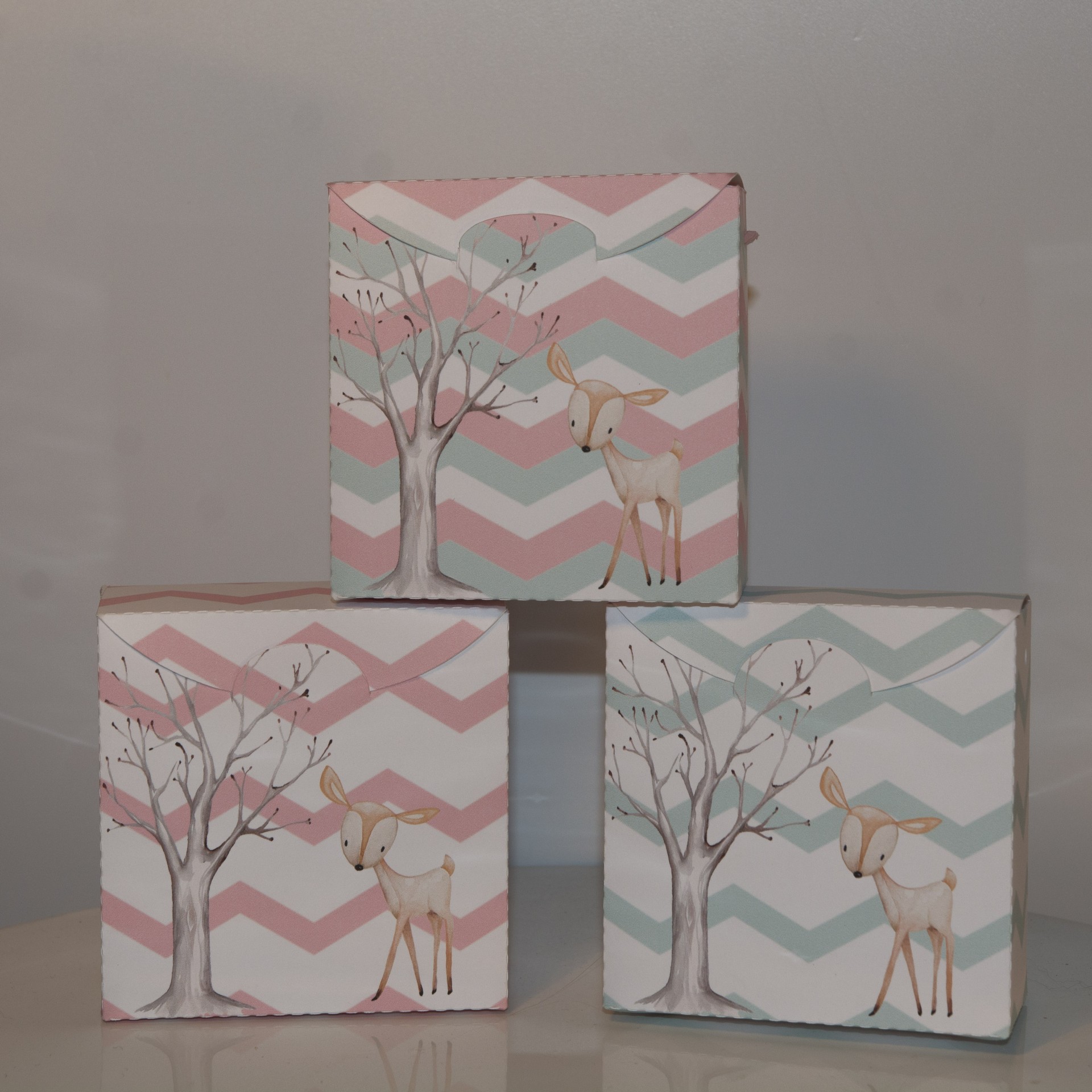 Três quadros decorativos com padrão zig-zag e ilustração de árvore e veado em tons pastéis.