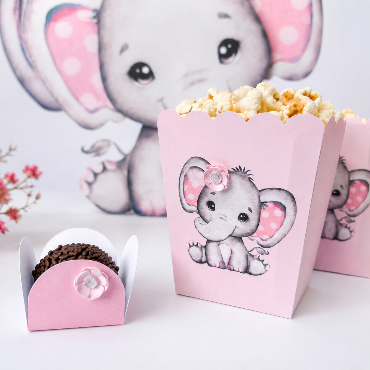 Caixas rosa decoradas com elefante e flor, uma com pipocas e outra com brigadeiro de chocolate.