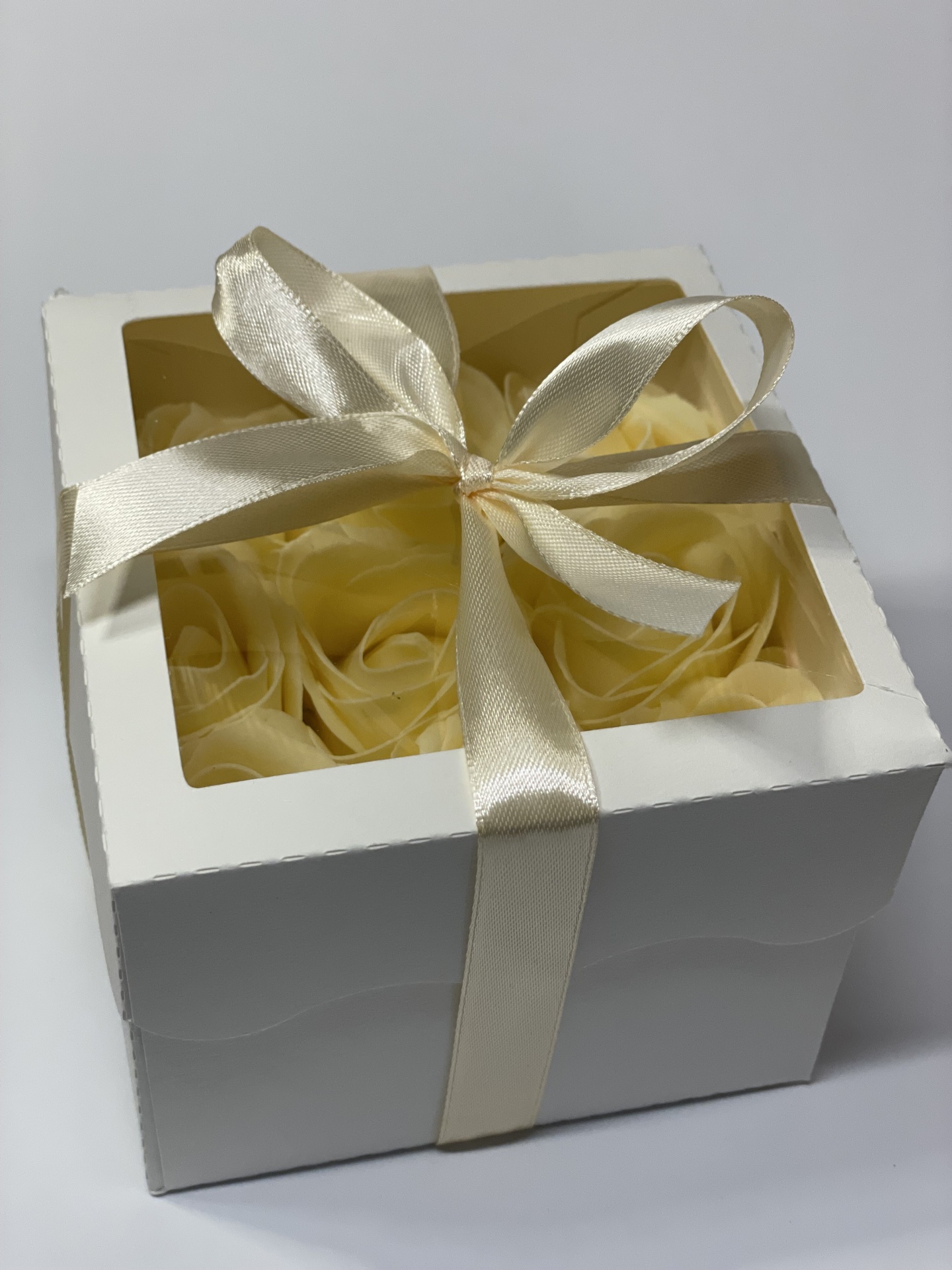 Caixa branca com flores amarelas artificiais e fita de cetim bege clara amarrada