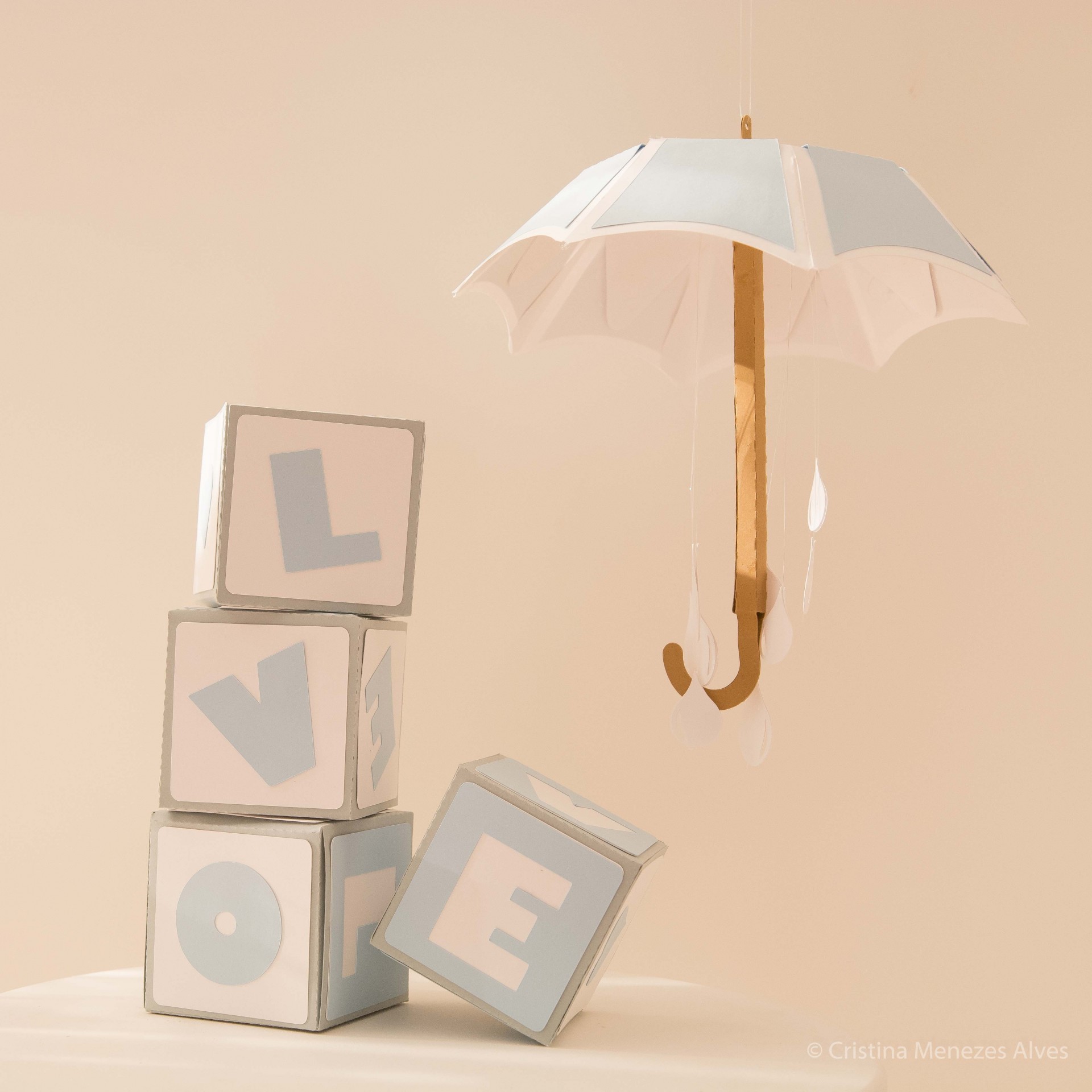 Cubos com letras formando LOVE ao lado de guarda-chuva branco suspenso num fundo castanho claro