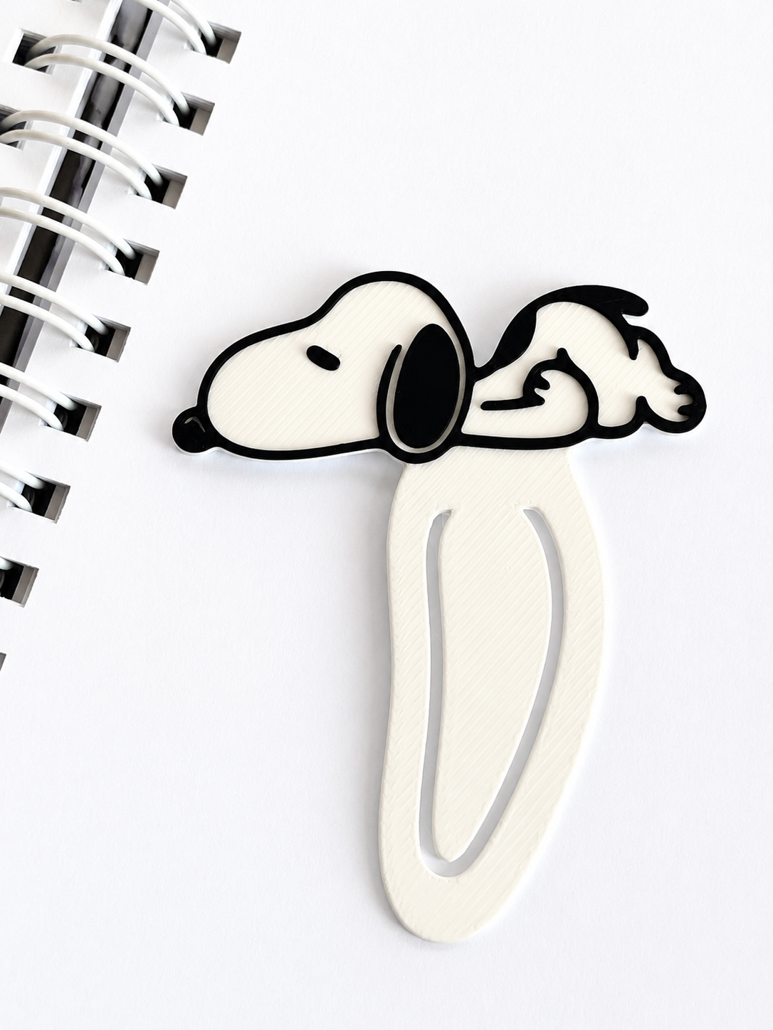 Marcador de página Snoopy de plástico sobre folha branca de caderno espiral metálico