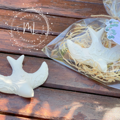 Pássaros decorativos brancos em cerâmica com padrões em relevo, embalagem em saco plástico sobre madeira escura