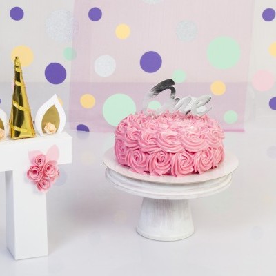 Bolo rosa decorado ao lado de número 1 decorativo e fundo com bolinhas coloridas